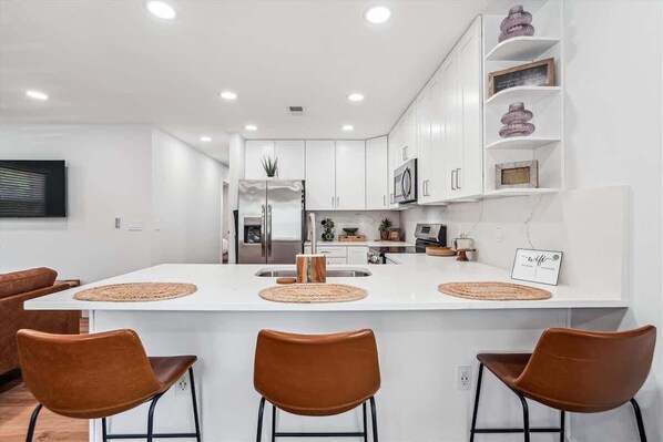 A modern kitchen with white cabinetry, a central island with bar stools, and built-in appliances.