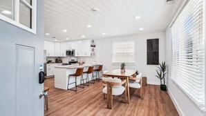 Een moderne keuken met witte kasten, een centraal eiland en een eethoek met houten stoelen.
