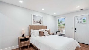 Een slaapkamer met een bed, nachtkastjes, een raam met jaloezieën en een deur.