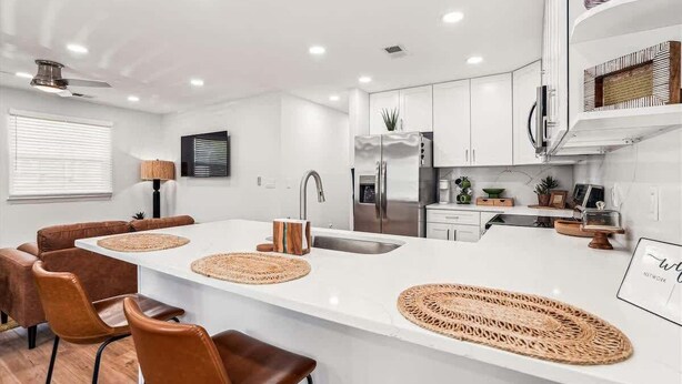 Een moderne keuken met witte kasten, een centraal eiland met geweven placemats en een eethoek met bruine lederen stoelen.