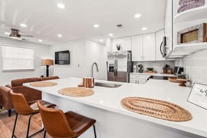 A modern kitchen with white cabinetry, a central island with woven placemats, and a dining area with brown leather chairs.