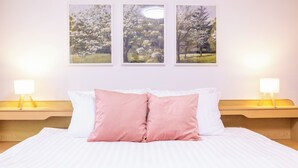 A neatly made bed with white and pink bedding, two bedside lamps, and three framed pictures on the wall.