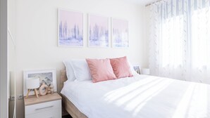 A bedroom with a bed, white nightstands, a bedside table with a lamp, and three framed pictures on the wall.