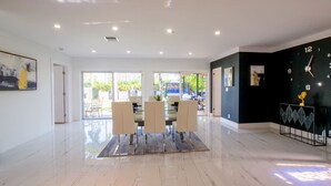 A spacious dining area with a modern table and chairs, a black clock on the wall, and a view through large windows. - Luxury 5BR/4BATH with Pool/Grill/Fire Pit/Parking (Hollywood)