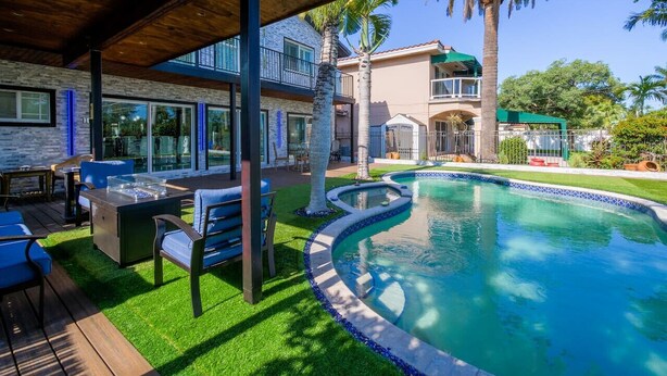A modern outdoor pool area with a wooden deck, blue chairs, and a fire pit. - Luxury 5BR/4BATH with Pool/Grill/Fire Pit/Parking (Hollywood)