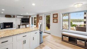 A modern kitchen with white cabinetry, granite countertops, and a view of a lake through large windows.
