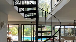 A modern interior with a spiral staircase, large windows, and a view of an outdoor swimming pool.
