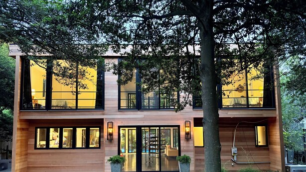 A modern two-story house with large windows, a wooden deck, and a well-maintained garden.