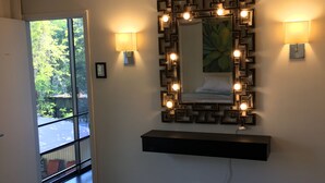 A room with a large mirror, wall-mounted lights, and a black shelf below it.