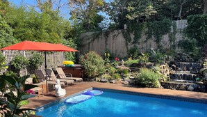 A backyard with a swimming pool, lounge chairs, a Buddha statue, and a small waterfall.