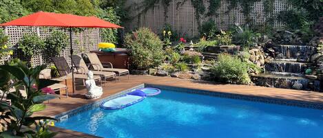 A backyard with a swimming pool, lounge chairs, a Buddha statue, and a small waterfall.