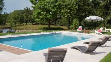 Ein rechteckiger Swimmingpool mit Liegestühlen und einem Sonnenschirm.