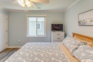 Une chambre à coucher avec un lit, un ventilateur de plafond, une fenêtre, une table de chevet et un tableau au mur.