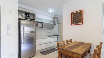 A compact kitchen with a stainless steel refrigerator, a microwave, and a gas stove. There is a wooden dining table with four chairs.