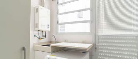 A laundry room with a washing machine, a drying rack, and a window with blinds.