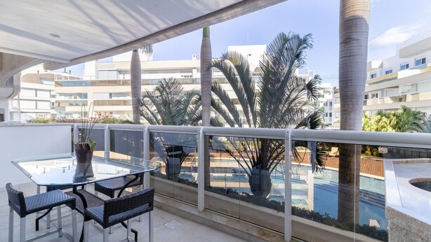 A balcony with a glass table and chairs, a potted plant, and a view of a swimming pool and buildings. - Apart w/ Barbecue in Condominium With Pool Bri0102 (Florianópolis)