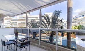 A balcony with a glass table and chairs, a potted plant, and a view of a swimming pool and buildings. - Apart w/ Barbecue in Condominium With Pool Bri0102 (Florianópolis)