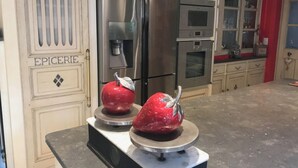 Eine Küche mit einem Edelstahl-Kühlschrank, einem Doppelbackofen und einer Küchenwaage, auf der zwei rote Äpfel liegen.