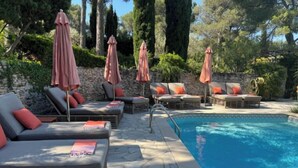 Ein Poolbereich mit Liegestühlen und Sonnenschirmen, einer terrassenförmig angelegten Fläche mit Steinplatten und einem klaren, blauen Pool.
