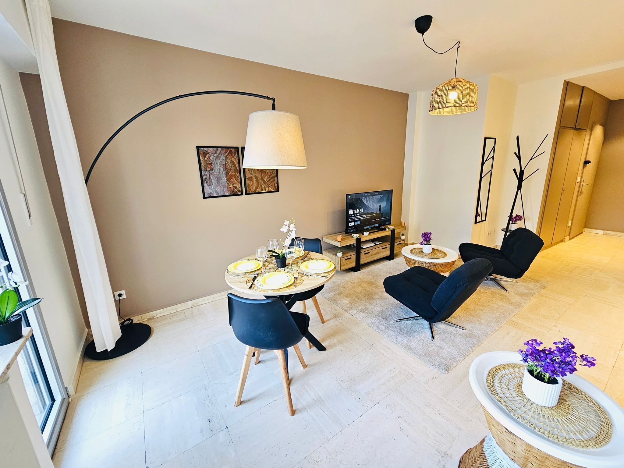 A modern living room with a dining table set for four, a sofa, a TV, and a floor lamp.