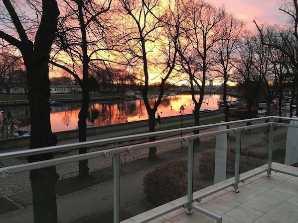 Une promenade au bord de la rivière, agrémentée d’une rambarde, d’arbres et d’un coucher de soleil en arrière-plan.