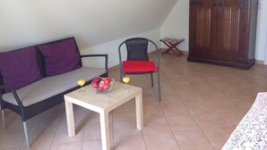 A room with a sofa, a dining table with fruit and drinks, a chair, and a cabinet. - Helle Wohnung mit Balkon am Strom in Warnemünde (Rostock)