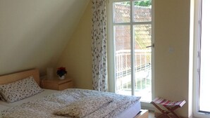 Un dormitorio con una cama de madera, una mesita de noche con un jarrón, una ventana con cortinas y una puerta que da al exterior.