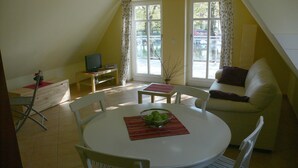 A small, well-lit room with a dining table, chairs, a sofa, and a television on a stand. - Helle Wohnung mit Balkon am Strom in Warnemünde (Rostock)