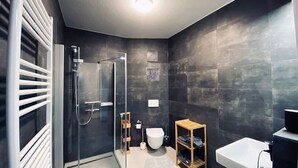 A modern bathroom with a glass shower enclosure, a white toilet, and a wooden shelf. - Warnowperle (Rostock)