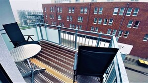 A balcony with two chairs and a small round table, overlooking a brick building with multiple windows. - Warnowperle (Rostock)