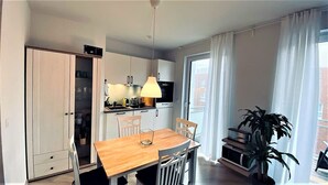 A modern kitchen with white cabinets, a wooden dining table, and a large window with curtains. - Warnowperle (Rostock)