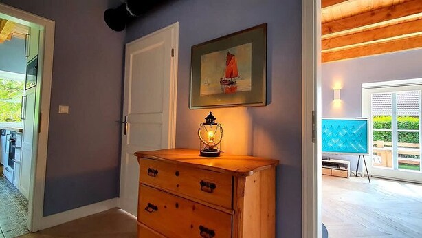 A hallway with a wooden dresser, a door, and a framed picture of a sailboat.