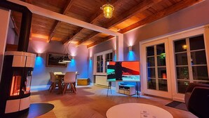 Un salon chaleureux avec une cheminée, un coin repas et un écran de télévision diffusant une scène hivernale enneigée.