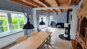 Un espace repas avec une table et des chaises en bois, une cheminée et de grandes fenêtres.