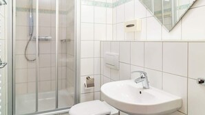 A bathroom with a glass shower enclosure, a white toilet, and a white sink with a mirror above it. - Krusenstern (Rostock)