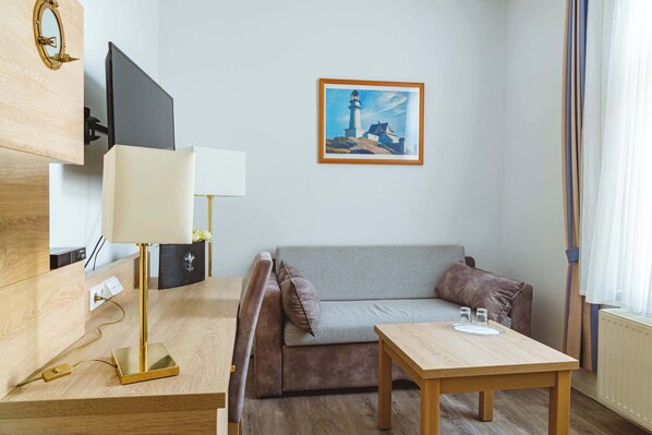 A hotel room with a wooden desk, a television, a sofa, a table with salt and pepper shakers, and a painting of a lighthouse.
