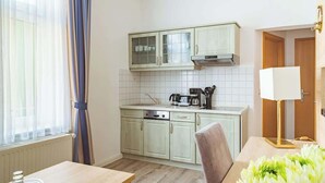 A compact kitchen with light green cabinets, a coffee maker, and a dining table with a vase of flowers. - Krusenstern (Rostock)