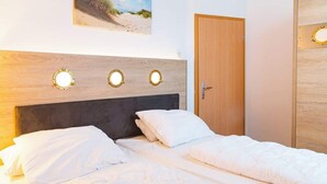 A bedroom with a wooden headboard, three wall-mounted lights, a door, and a framed picture on the wall. - Krusenstern (Rostock)