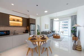 A modern kitchen with a dining area, a living room with a sofa and a coffee table, and a view of a balcony.