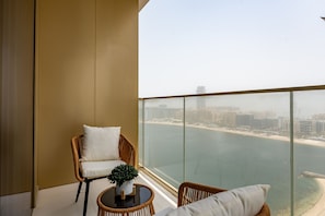 A balcony with wicker furniture, a potted plant, and a view of a coastal cityscape.