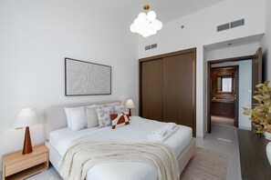 A modern hotel room with a large bed, bedside tables with lamps, a wooden wardrobe, a bathroom visible through an open door, and a decorative plant.