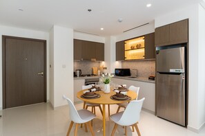 A modern kitchen with a dining area, featuring a stainless steel refrigerator, wooden cabinets, and a round dining table with chairs.