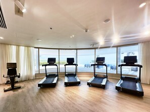 Un gimnasio con cuatro cintas de correr, ventanas amplias y un ventilador de techo.