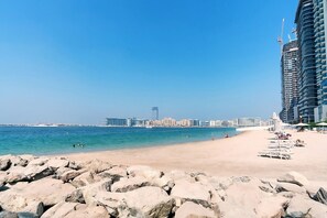 Una playa con un primer plano rocoso, una orilla arenosa y el horizonte de una ciudad al fondo.