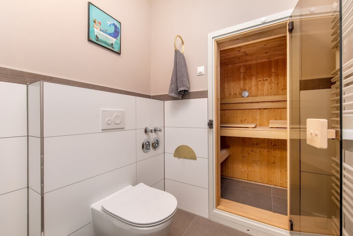 A modern bathroom with a white toilet, a glass shower enclosure, and a wooden sauna.