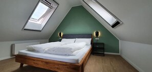 Een slaapkamer met een schuine kap, dakraam, houten bed en witte beddengoed, met twee wandlampen.