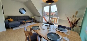Een eethoek met een houten tafel voor vier personen, een grijze bank en uitzicht op buiten.
