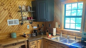 A wooden cabin kitchen with a wooden countertop, a sink, a stove, and cabinets.