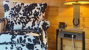 A room with a cow print armchair, a lamp with a horse silhouette, and a painting of horses on the wall.