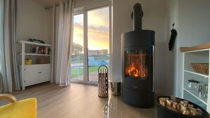 Ein gemütliches Wohnzimmer mit Kaminofen, Bücherregal und Blick ins Freie.